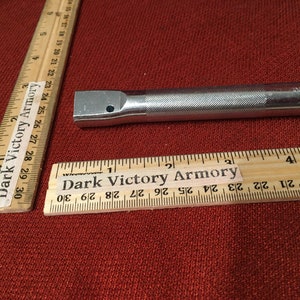 Puede incluir: Una extensi&oacute;n de llave de metal plateado con un mango moleteado y un extremo cuadrado de accionamiento. La extensi&oacute;n mide aproximadamente 10 cm de largo. La regla en la imagen est&aacute; marcada con "Dark Victory Armory".