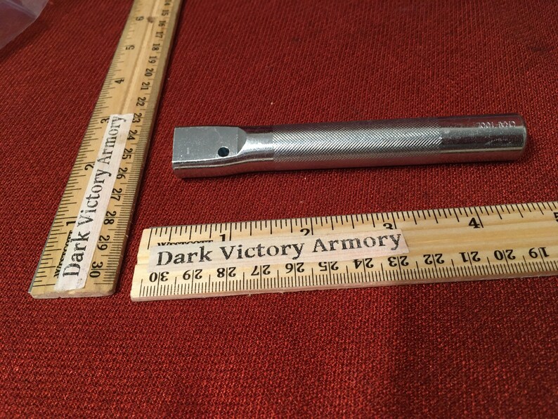 Puede incluir: Una extensi&oacute;n de llave de metal plateado con un mango moleteado y un extremo cuadrado de accionamiento. La extensi&oacute;n mide aproximadamente 10 cm de largo. La regla en la imagen est&aacute; marcada con "Dark Victory Armory".
