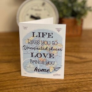 May include: A card with a world map background and the text "LIFE takes you to unexpected places LOVE brings you home".