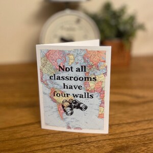 May include: A white card with a vintage world map background. The text "Not all classrooms have four walls" is printed in black. A pair of black binoculars is centered below the text.