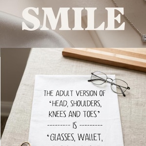 May include: A white rectangular kitchen towel featuring black printed text that reads: THE ADULT VERSION OF 'HEAD, SHOULDERS, KNEES AND TOES' -------- IS -------- 'GLASSES, WALLET, KEYS AND PHONE.' The fabric is plain white with a simple sans-serif font.