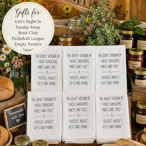 photograph showcasing six of these premium towels in a shingle display on a rustic wooden farmhouse table. The scene should is enriched with artisan jellies and freshly baked homemade breads, capturing the warm, abundant atmosphere of a Sunday swap harvest exchange aesthetically pleasing text overlay reads: Gifts for: Girl's Night In, Sunday Swap, Book Club, Pickleball League, Empty Nesters The Adult Version Of Head, Shoulders, Knees Toes is Glasses Wallet Keys Phone Kitchen Tea Towel