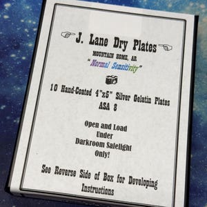 May include: A rectangular box of J. Lane Dry Plates containing 10 hand-coated 4"x5" silver gelatin plates with ASA 8 sensitivity. The white label features black text, pointing finger icons, a camera icon, and instructions to open under darkroom safelight.