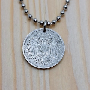 Può includere: Collana con catena d'argento con un ciondolo a forma di moneta d'argento che presenta un'aquila bicipite con una corona in cima.