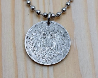 Könnte beinhalten: Silberkette mit einem silbernen Münzenanhänger, der einen Doppelkopfadler mit einer Krone auf dem Kopf zeigt.