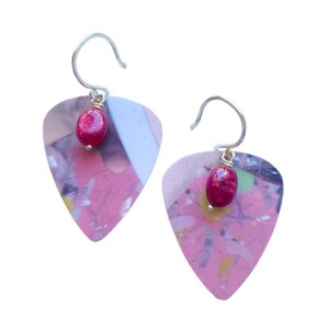 May include: A pair of earrings with a pink and white guitar pick design and a red gemstone hanging from each pick.