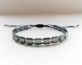 Puede incluir: Un brazalete negro con cuentas cuadradas y cierre de cordón negro.