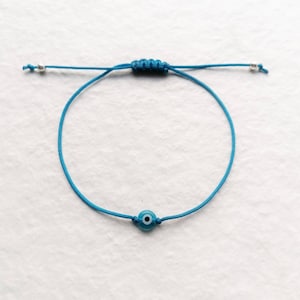 Puede incluir: Un brazalete de cuerda azul con un pequeño amuleto azul de ojo turco.