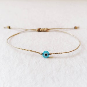 Puede incluir: Un brazalete simple de cuerda con un dije azul de ojo turco. El brazalete está hecho de fibra natural y es ajustable.