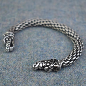 May include: A silver bracelet with two wolf head ends. The bracelet is made of a chain link design.