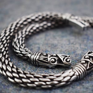 May include: A silver chain bracelet with a detailed, ornate clasp. The clasp is shaped like a dragon's head with intricate designs.