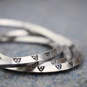 May include: Three silver bangles with a geometric pattern of triangles and dots. The bangles are stacked on top of each other.