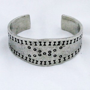 May include: A silver bracelet with a geometric pattern of black circles and X shapes.