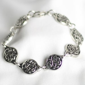 May include: A silver bracelet with a chain link design and oval-shaped charms. Each charm features an intricate Celtic knot design.