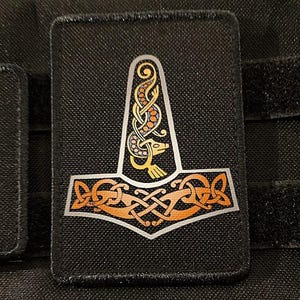 May include: A black fabric patch with a gold and orange embroidered design of a stylised hammer with a serpent-like head. The hammer is surrounded by a Celtic knot design.