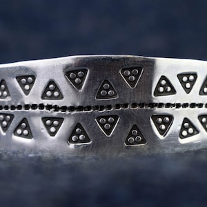 May include: A silver bracelet with a repeating pattern of triangles and dots.