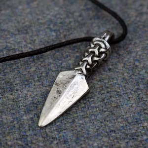 May include: A silver pendant in the shape of a spearhead with a Celtic knot design at the top. The pendant is on a black cord.