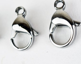 May include: Two silver metal lobster claw clasps, one larger than the other, on a white background.