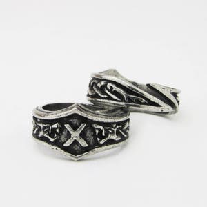 May include: Two silver rings with intricate designs. One ring features a stylized 'X' and the other has a swirling pattern.
