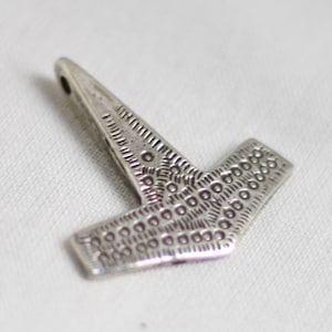 May include: Silver pendant in the shape of a hammer with a detailed patterned design.