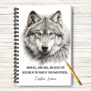 May include: A white notebook with a black and white drawing of a wolf's head. The notebook has a spiral binding and the text "DREAM BIG, WORK HARD, AND NEVER STOP BELIEVING IN THE POWER OF YOUR OWN POTENTIAL." and "Custom Name" are printed on the cover.