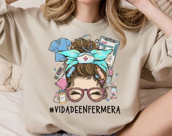 May include: A beige sweatshirt with a graphic of a woman with a messy bun, wearing a nurse's hat and glasses. The graphic includes medical supplies and the text "#VIDADEENFERMERA".