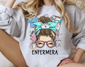 May include: A gray sweatshirt with a graphic of a woman with a messy bun, wearing glasses and a nurse's hat. The graphic includes medical supplies and the word "ENFERMERA".