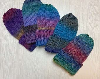 May include: Five hand-knitted beanies in a variety of colors are displayed. Each beanie features a gradient of colors, including purple, blue, green, and pink. The beanies are made of a soft, textured yarn.