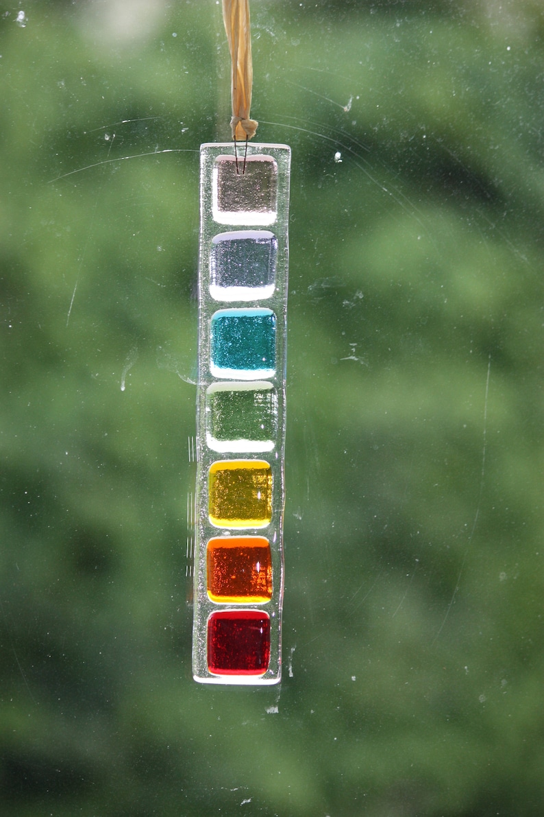 May include: A glass suncatcher with a series of colored squares. The squares are in the colors of the rainbow, starting with red at the bottom and ending with purple at the top.