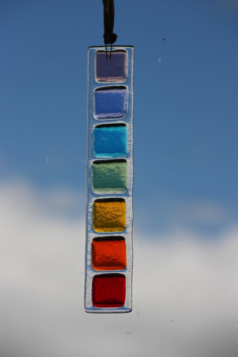 May include: A stained glass suncatcher with a rainbow of colors. The suncatcher is made of glass squares in shades of purple, blue, green, yellow, orange, and red.