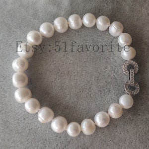 May include: A white pearl bracelet with a silver clasp. The bracelet is made of large, round pearls. The clasp is silver and has a decorative design. The text "Etsy: 51favorite" is visible.