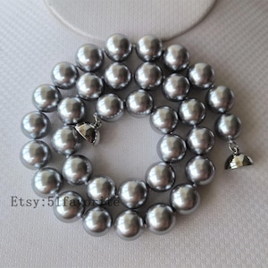 Peut inclure: Un collier de perles argentées avec un fermoir argenté. Les perles sont grandes et rondes.