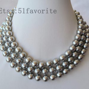 Puede incluir: Collar de perlas gris plateado de tres hilos. El collar se exhibe sobre un busto de maniquí blanco. Las perlas son redondas y de tamaño uniforme, con un brillo lustroso. El texto "Etsy: 51favorite" es visible en la esquina superior izquierda.