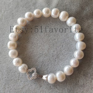 May include: A white pearl bracelet with a silver clasp. The bracelet is made of large, irregularly shaped pearls. The clasp is a clover shape with small, clear stones. The text "Etsy: 51favorite" is visible.