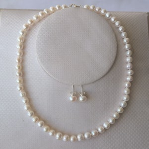 以下が含まれることがあります： 白い真珠のネックレスとそれに合うイヤリング。ネックレスは小さく丸い真珠でできており、銀のチェーンに通されています。イヤリングも小さく丸い真珠でできており、銀のポストに付いています。