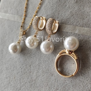 May include: A gold-toned jewelry set featuring a necklace, earrings, and a ring. The necklace and earrings have a dangling white pearl. The earrings and necklace have a small, sparkling stone design. The ring has a large white pearl.