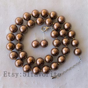 May include: A bronze-coloured pearl necklace and matching stud earrings set. The necklace features large, round pearls strung with gold-toned spacers. The earrings have similar bronze pearls. The Etsy shop name "51favorite" is visible.