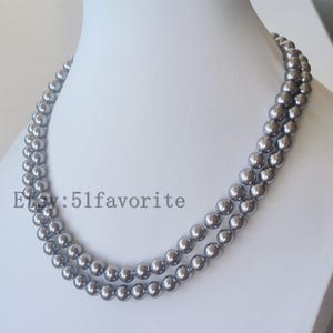 Puede incluir: Un collar de perlas grises de doble hebra exhibido en un maniquí blanco. Las perlas son redondas y de tamaño uniforme, con un brillo lustroso. El nombre de la tienda Etsy "51favorite" es visible.