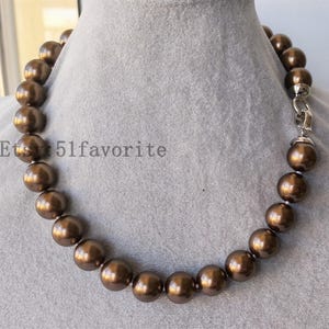Op de afbeelding: Een bruine kralenketting met een zilveren sluiting. De ketting heeft grote, ronde kralen in een rijke, chocoladebruine kleur. De kralen zijn aan elkaar geregen, waardoor een opvallend sieraad ontstaat. De tekst "Etsy 51favorite" is zichtbaar.