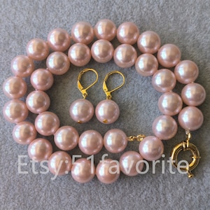 以下が含まれることがあります： 淡いピンクの真珠のネックレスとイヤリングのセット。ネックレスは大きく丸い真珠で作られており、金色の留め具が付いています。イヤリングも大きく丸い真珠で作られており、金色のフックが付いています。