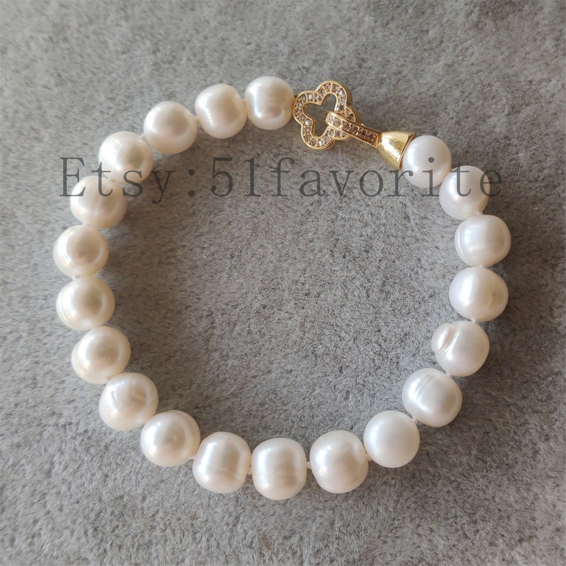 May include: A white pearl bracelet with a gold-colored clasp. The bracelet is made of large, round pearls. The clasp is shaped like a four-leaf clover and is encrusted with small, clear stones. Text on the image reads "Etsy: 51favorite".
