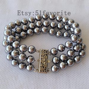 Puede incluir: Una pulsera de tres hilos con cuentas redondas grises. La pulsera tiene un cierre decorativo plateado. El texto "Etsy: 51favorite" es visible en la parte superior de la imagen.