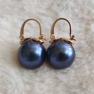 Op de afbeelding: Een paar gouden oorringen met donkerblauwe parelhangers.