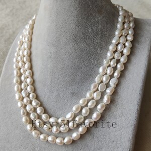 May include: A triple strand pearl necklace with white, round pearls. The necklace is on a white background.