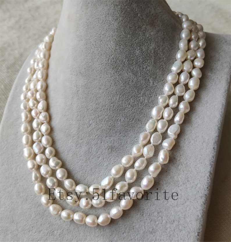 May include: A triple strand pearl necklace with white, round pearls. The necklace is on a white background.