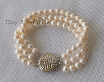 May include: A white pearl bracelet with a silver clasp featuring a traditional Chinese symbol. The bracelet is made of three strands of pearls.
