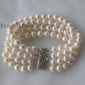 Può includere: Un braccialetto di perle bianche con una chiusura argentata. Il braccialetto è composto da quattro file di perle.