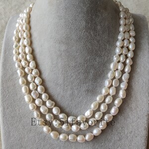 May include: A triple strand pearl necklace with white, round pearls. The necklace is on a gray background.