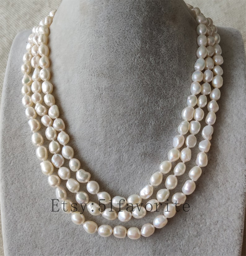 May include: A triple strand pearl necklace with white, round pearls. The necklace is on a gray background.