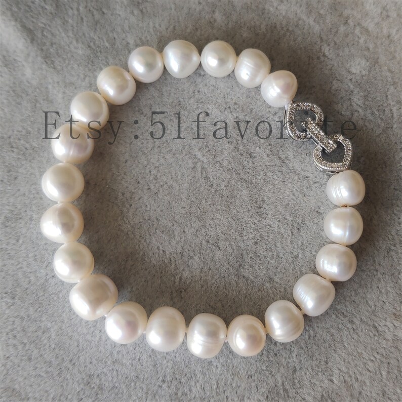 May include: A white pearl bracelet with a heart-shaped clasp. The bracelet features large, round pearls strung together. The clasp is silver and encrusted with small, clear stones. The Etsy shop name "51favorite" is visible in the image.